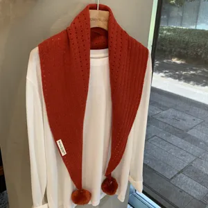 Detail view of the red knitted triangular scarf with delicate hollow-out pattern and cute pom-poms.
