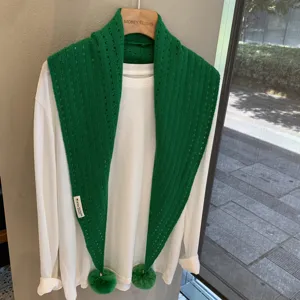 Green hollow knitted triangular scarf with cute pom-poms, stylish wool shawl for women detail view.