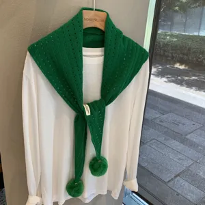 Detailed shot of the green knitted hollow-out triangle scarf shawl with cute pom-poms.