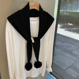 Detail shot of black knit triangular scarf with pom poms layered on white long sleeve tee.