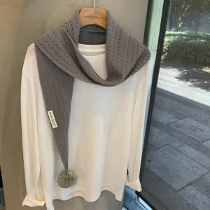 Close-up detail of grey knitted hollow-out triangle scarf with pom-pom and white layered top