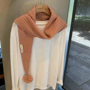 Detailed view of pink knitted triangle scarf with pom-pom, wool blend, stylish layering accessory.