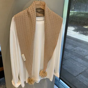 Beige knitted triangular scarf with pom-poms, wool blend hollow shawl, versatile winter accessory.