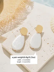 Detailed shot of French textured gold and white imitation pearl drop earrings on stone.