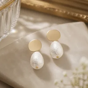 Detailed view of French style gold disc and textured faux pearl drop earrings for women.