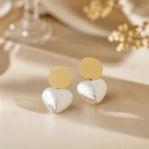 Close-up view of French gold disc and textured white heart pearl earrings, elegant accessory.
