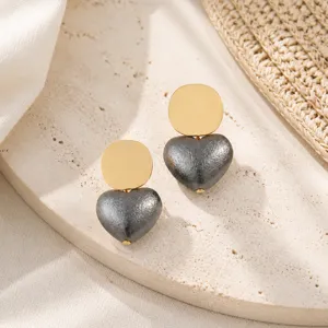Close-up shot of retro geometric gold-tone disc and textured dark grey heart dangle earrings.