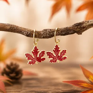 Detailed shot of autumn red enamel maple leaf drop earrings hanging on a rustic branch.