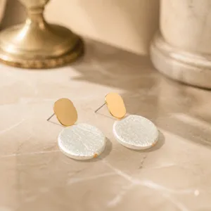 Close-up detail view of elegant French style textured white disc earrings with chic gold studs.