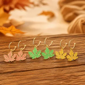 Close-up details of autumn maple leaf hoop earrings in pink, green, and yellow enamel styles.