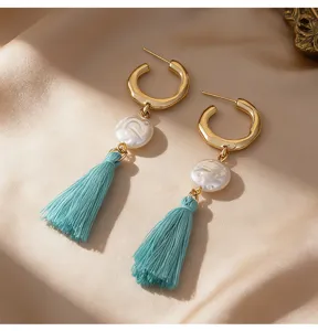 Gros plan détaillé de boucles d'oreilles créoles dorées avec perle et glands turquoise style bohème.