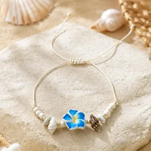 Détail de bracelet tressé bohème fait main avec fleur plumeria bleue et coquillages.