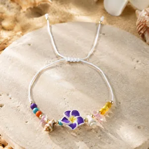 Détail de bracelet style bohème fait main avec breloques fleur mauve et coquillages.