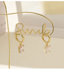 Gros plan détaillé de boucles d'oreilles en zircon doré 14K élégantes avec un design script smile.