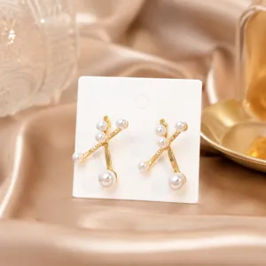 Detailaufnahme minimalistischer Kreuz-Ohrringe mit weißen Perlen auf goldenem Metall.