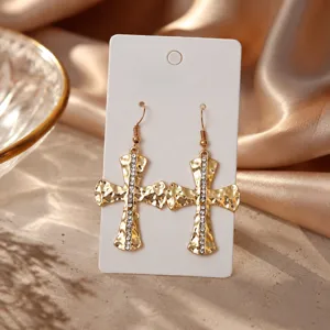 Detailaufnahme trendiger goldener gehämmerten Kreuz-Ohrringe mit Strass auf Präsentationskarte.