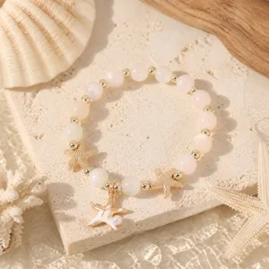 Detailaufnahme des stilvollen Katzenauge Perlenarmbands mit goldenen Seesternen am Strand.