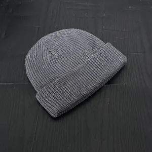 Close-up detail of a grey knitted beanie, showing fine ribbed texture and short dome shape.