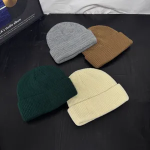 Close-up detail of four colorful knit beanies in grey, brown, green, and beige for winter.