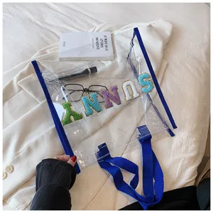 Transparente PVC-Einkaufstasche mit bunten Buchstaben-Aufnähern und blauem Rand für den Strand.