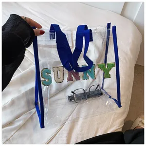 Transparente PVC Strandtasche mit blauen Griffen und bunten Buchstaben für den Sommer.