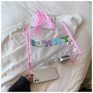 Detailaufnahme der klaren PVC Strandtasche mit rosa Henkeln und bunten Buchstaben Applikationen.