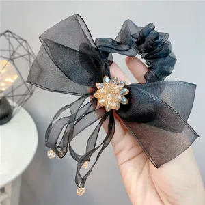 Detail van zwarte organza haarelastiek met champagnekleurige kristallen bloem en lint.
