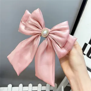 Close-up of pink satin bow hair clip with pearl rhinestone centerpiece and long ribbons.