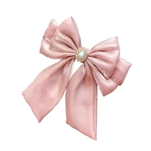 Detailed view of pink satin bow hair clip with pearl rhinestone center and long ribbons.