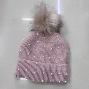 Close-up detail of the pink knitted beanie featuring white pearls and a fluffy pom-pom top.