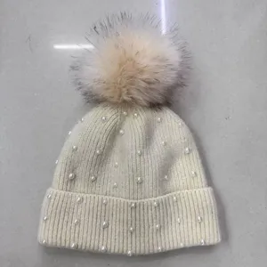 Detailed view of women winter knit beanie hat featuring pearl decor and fluffy fur pom.