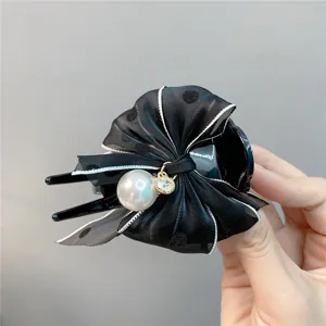 Detailed close-up of a stylish black hair claw clip featuring a polka dot bow and pearl.