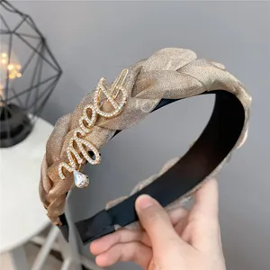 Shimmering gold braided headband with rhinestone script brooch, elegant fashion hair accessory.