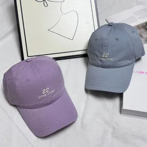 Detail view of washed cotton baseball caps in purple and gray with stylish embroidery.