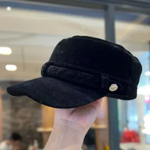 Detailopname van een zwarte corduroy platte pet met gestructureerde stof en metalen knop.