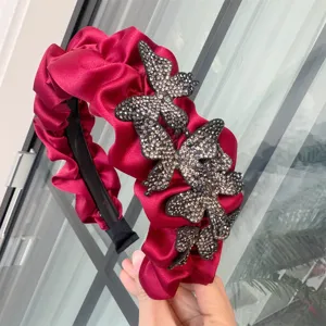 Nahaufnahme eines roten Satin Haarreifs mit Falten und funkelnden Strass Schmetterling Details.