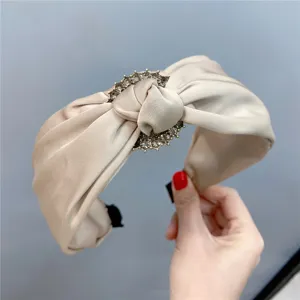 Detail view of a chic champagne satin headband with rhinestone buckle and elegant knot.