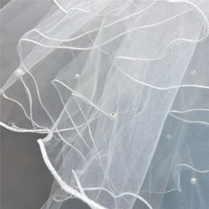Close-up detail of white bridal veil tulle fabric featuring wavy decorative lines and pearls.
