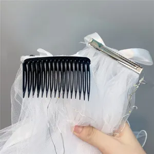 Detailed close-up shot of white mesh bridal hair veil with black comb and metal clip.