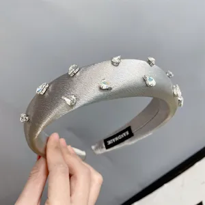 Detailed shot of a silver satin padded rhinestone headband with crystal droplets and label.