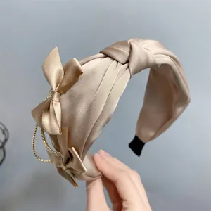 Close-up detail of champagne satin knotted headband with sweet bow and delicate pearl tassel.