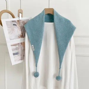 Détail de l'écharpe triangulaire tricotée bleue avec pompons, idéale pour l'hiver.