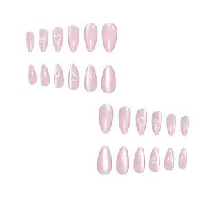 Detail view of long almond pink cat-eye press-on nails featuring cute white heart and bow art.