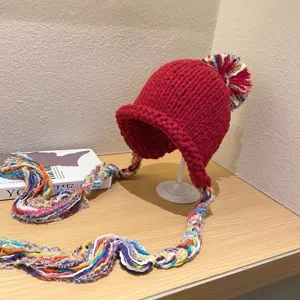 Red knitted beanie hat detail showcasing colorful braided tassels and fluffy pom-pom top.