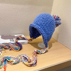 Detailed view of blue chunky knit beanie with colorful braided tassels and top pompom.