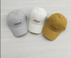 Detail view of embroidered baseball caps in grey white and khaki colors with ocean text.