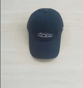 Close-up detail of the navy blue embroidered baseball cap featuring front ocean and mountain text design.