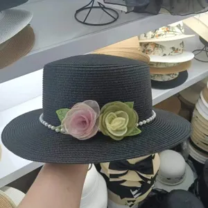 Detailansicht des eleganten schwarzen Strohhutes mit Blumen- und Perlendekor für den Strand.