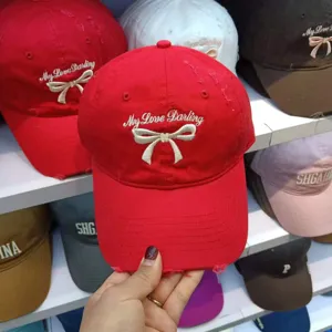 Detail view of red cotton baseball cap with cute embroidered bow and white letter design.