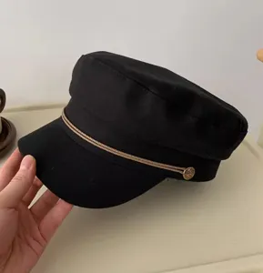 Schwarze flache Top Mütze Detailaufnahme mit doppelter Kordel und goldenem Seitenknopf.